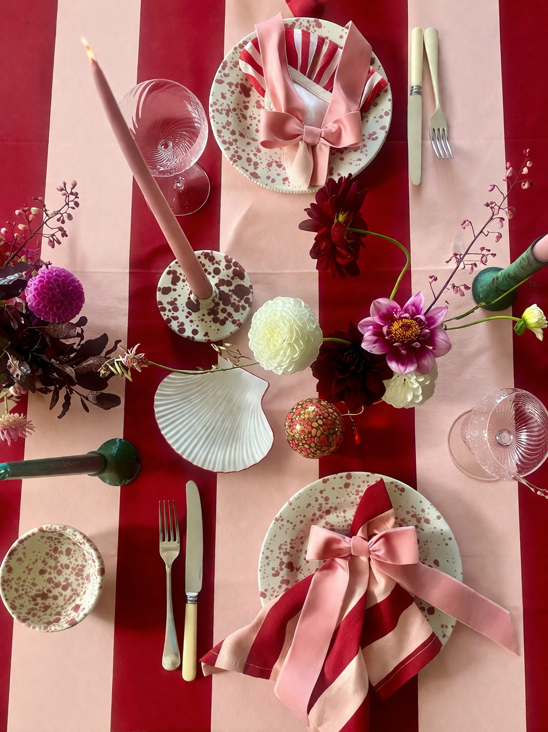 Decorative table setting with white shell plate with red outline, pink flowers, red splatter tableware on red and peach striped tablecloth
