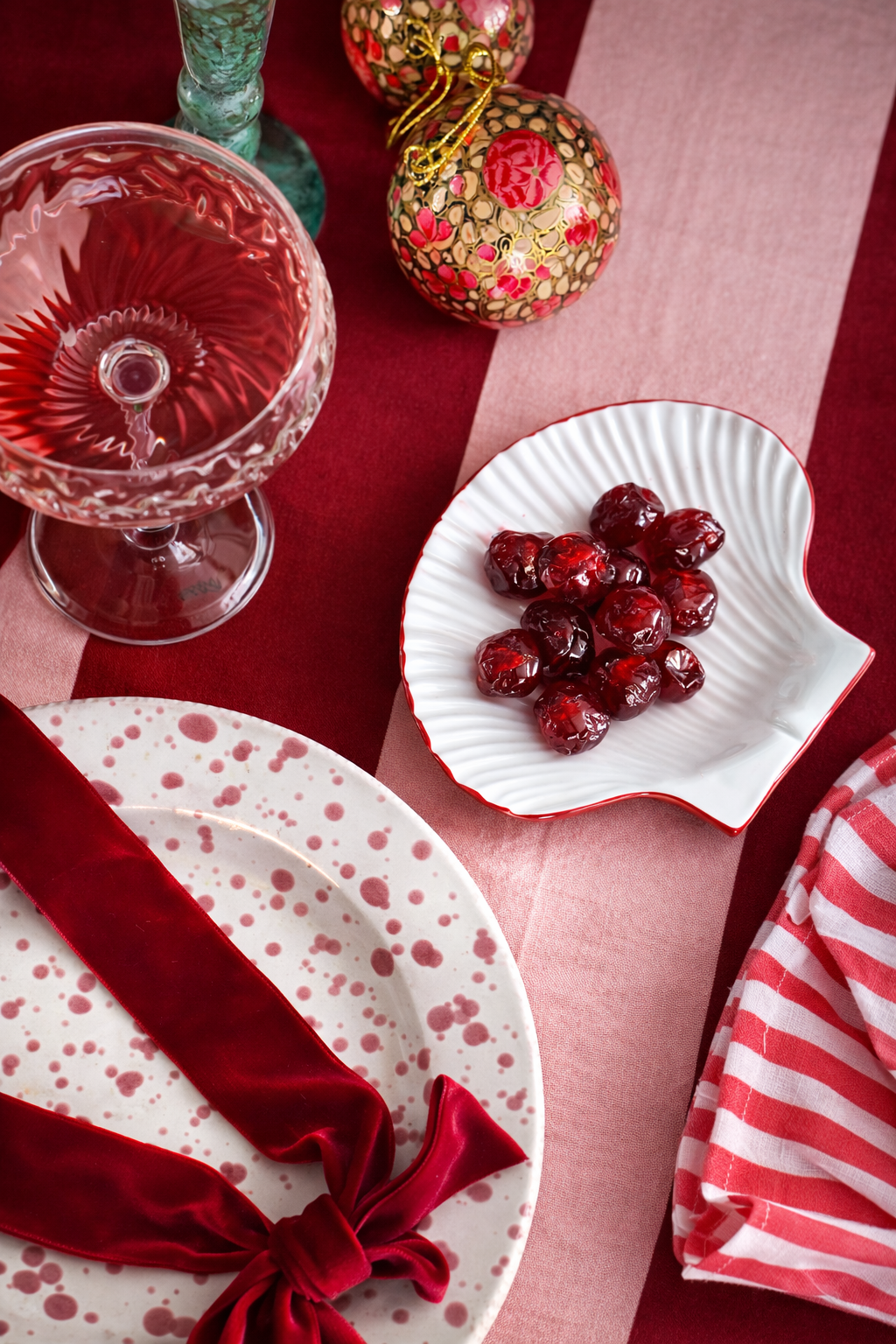 Decorative table setting with red and white elements, including a glass, plate with cherries, and striped napkin.
