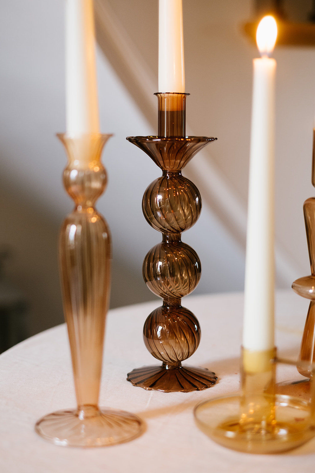 Close up of brown and rust coloured glass candleholders with candles lighting in cream room