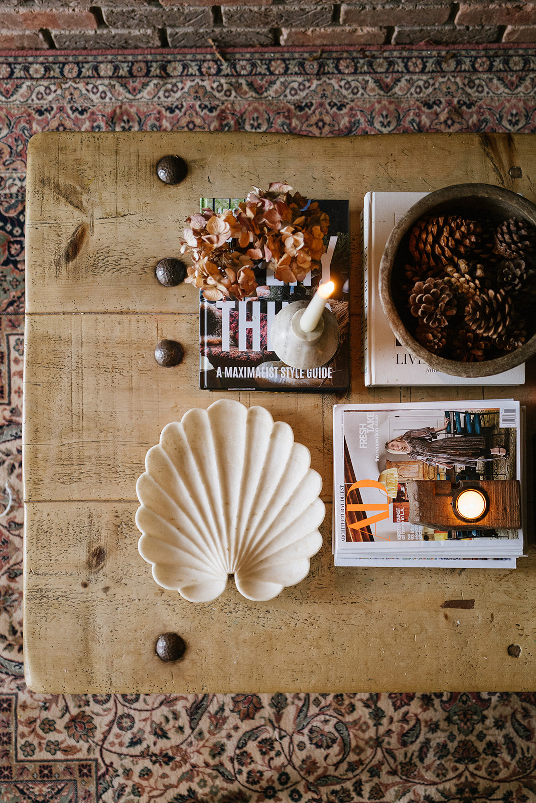 Overhead view of rustic wood cofee table setting with marble shell plate, bowl of pinecones, candles lighting