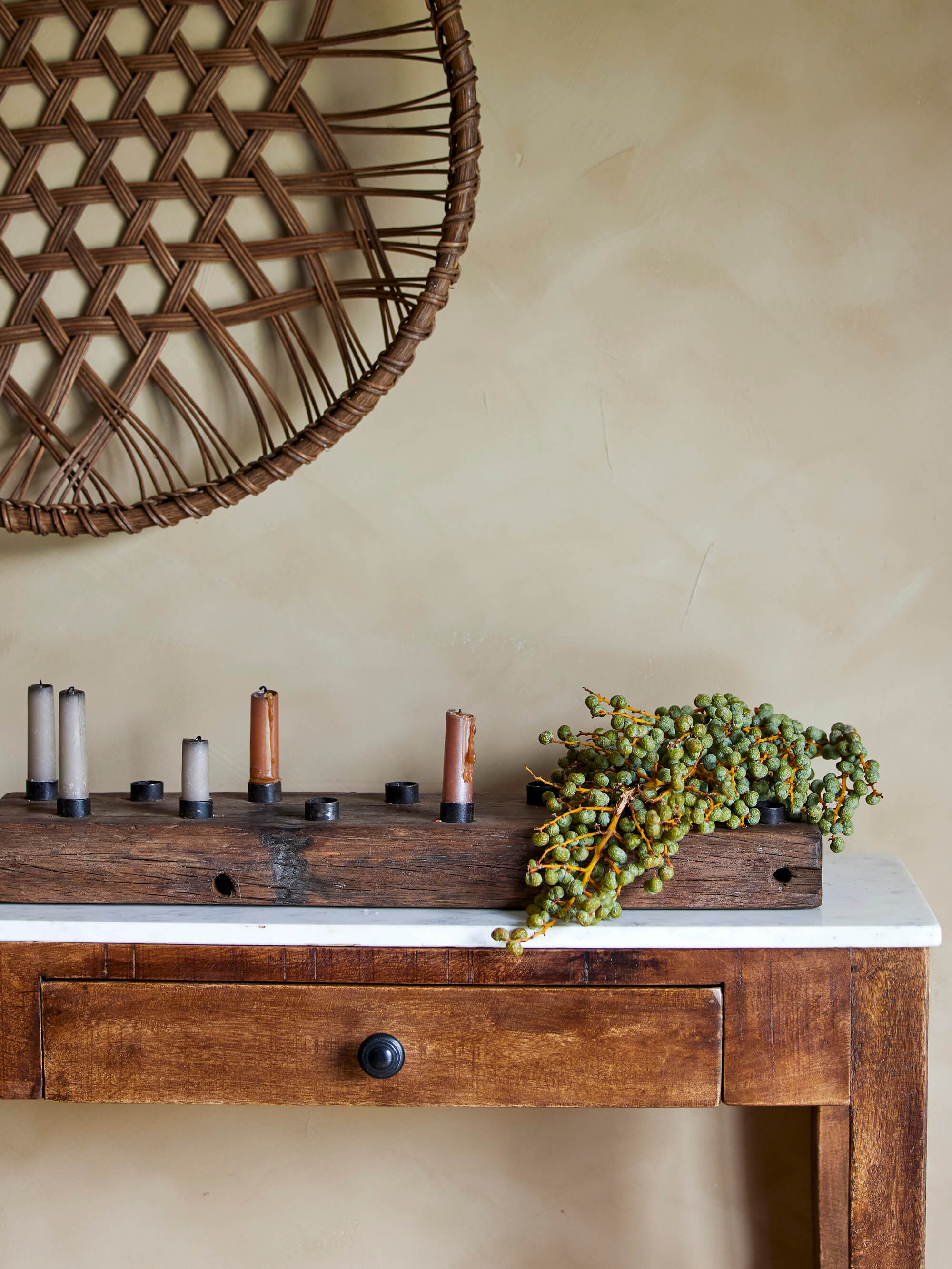 Reclaimed wood candle holder panel on a wooden condsole table against a taupe textured background and round woven decorate panel above