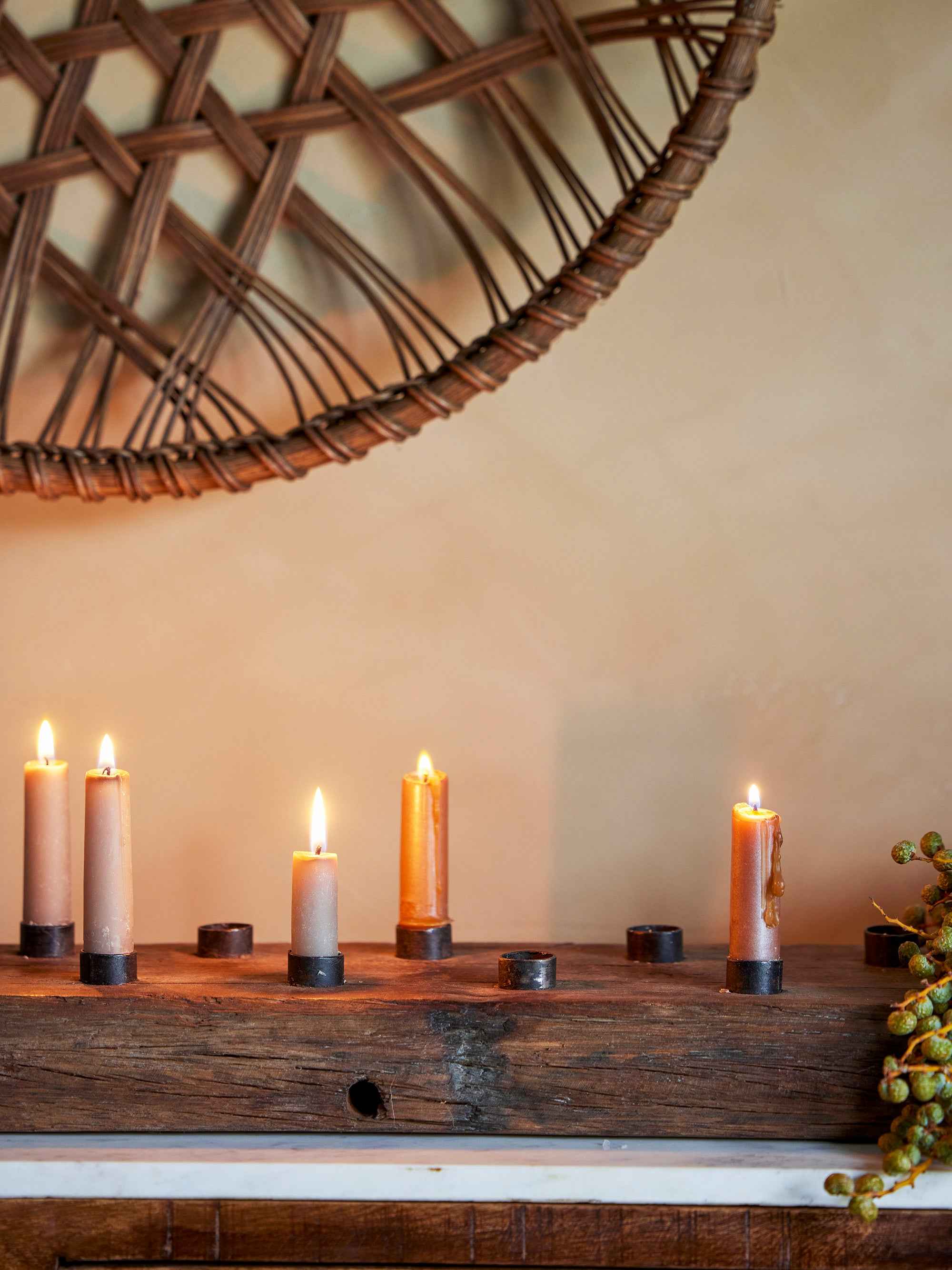 Candles burning in a rustic wooden plank candle holder panel with a woven decorative object above