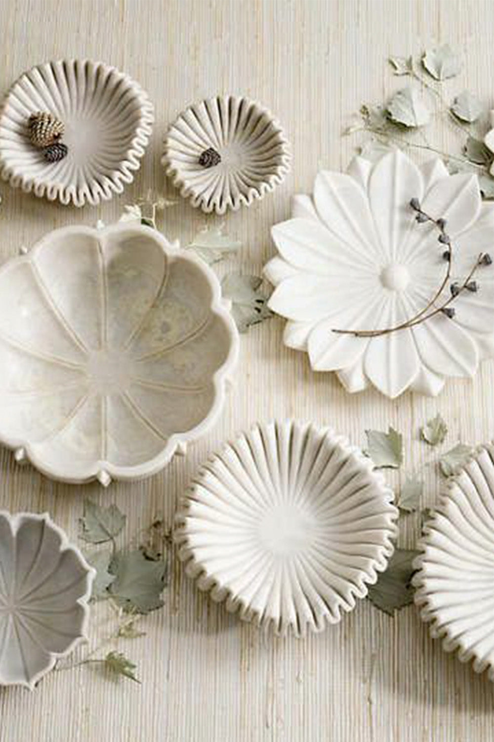 Overhead view of white sculptural bowls in different shapes finishes and sizes on a white textured background