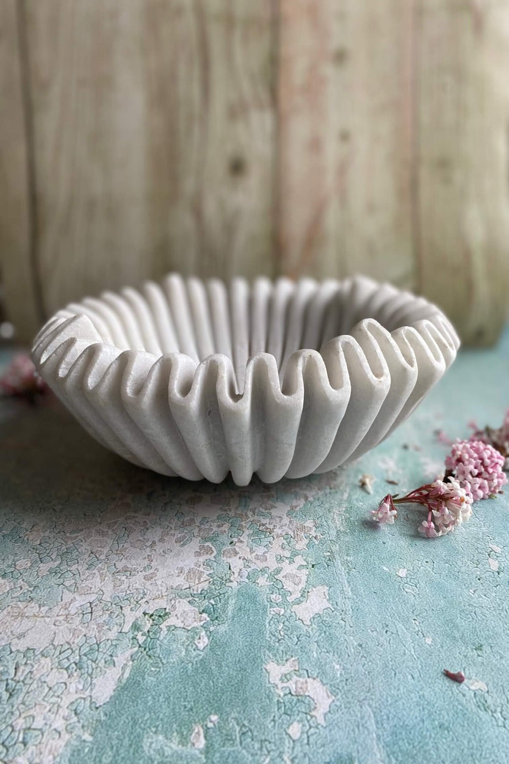 Front view of ruffled marble bowl on textured turquoise surface against rustic plank wall
