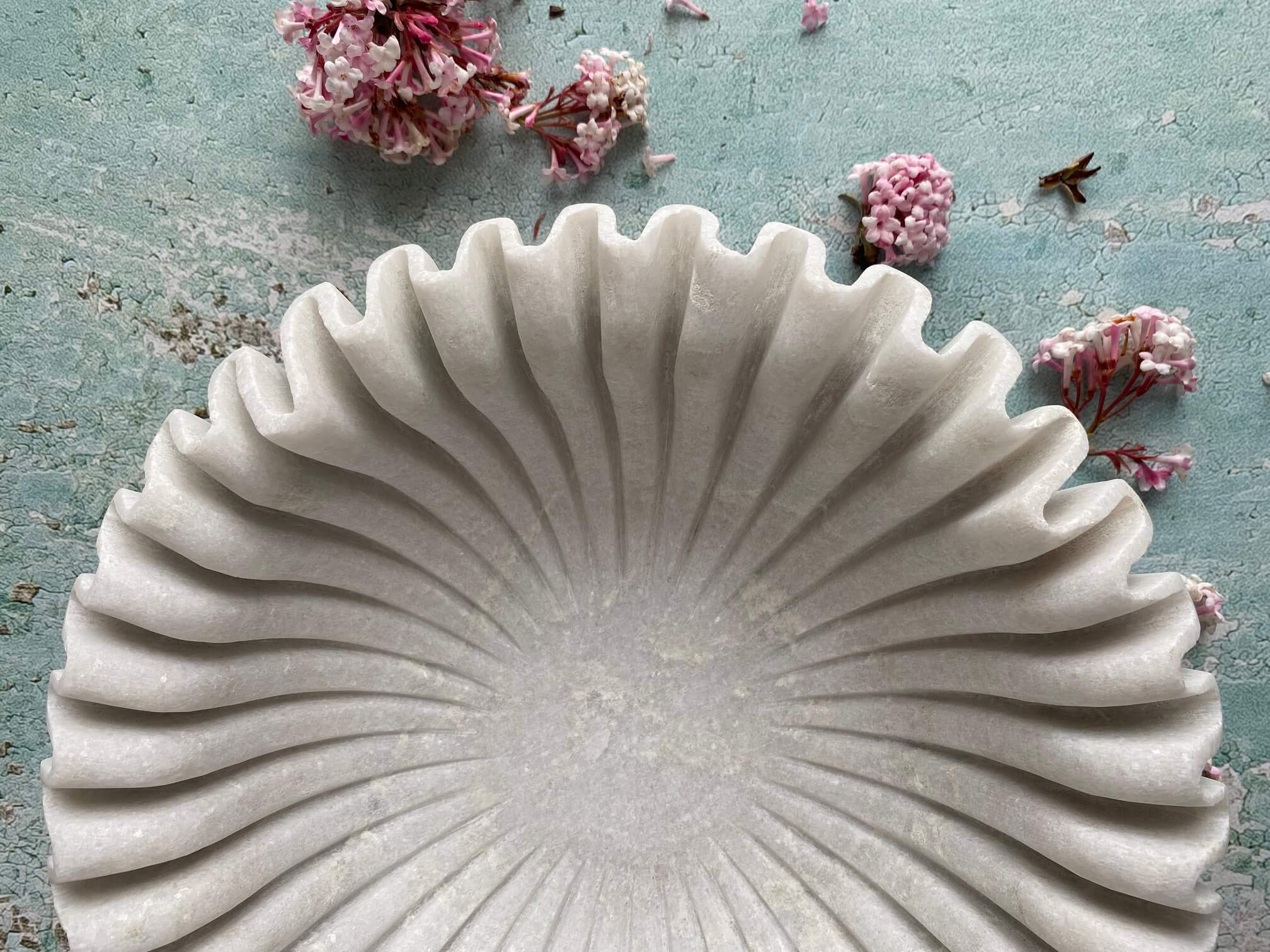 Close up shot of ruffled marble bowl on textured turquoise background with cherry blossom