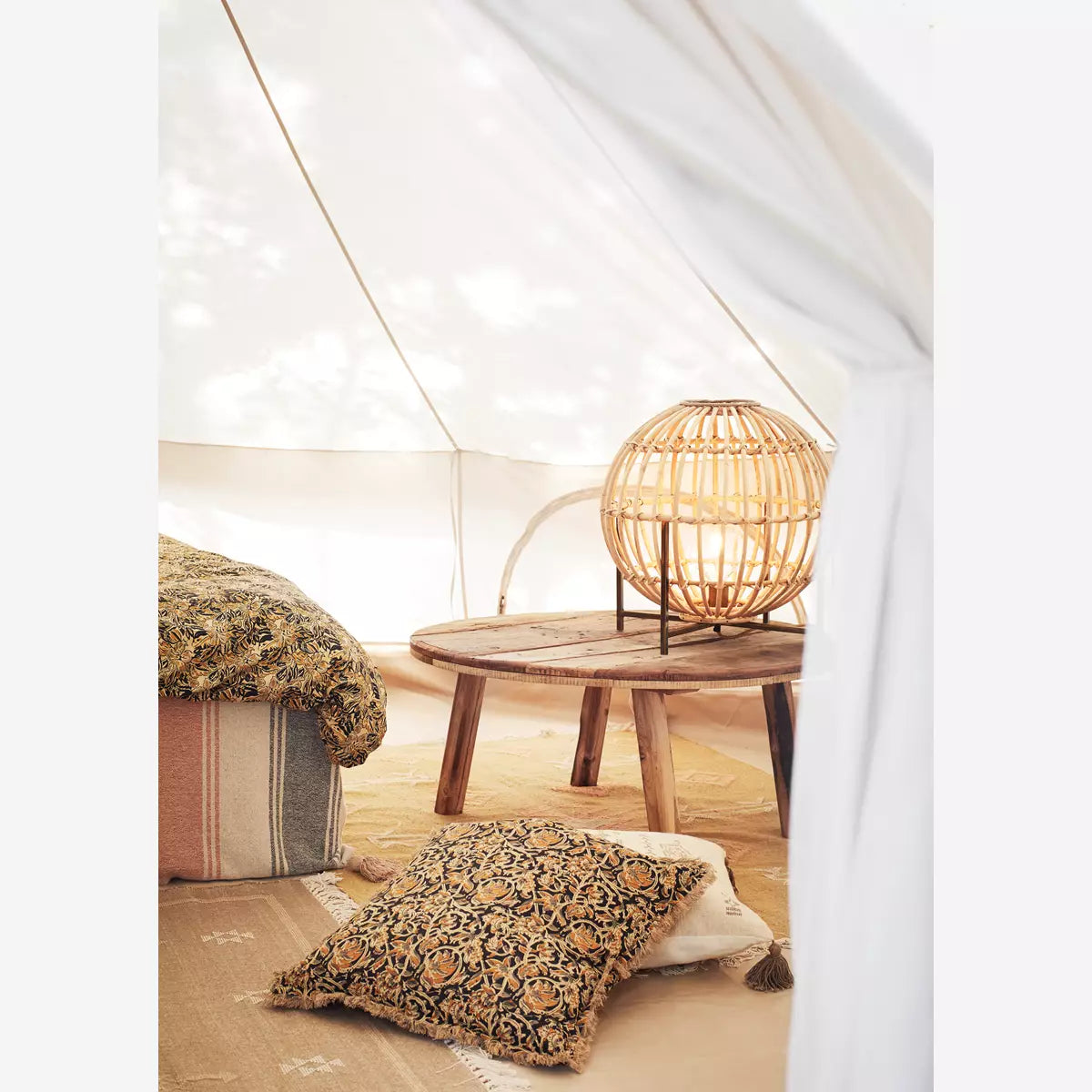 An image of reclaimed wood round coffee table in a bell tent with cushions and a rattan lamp