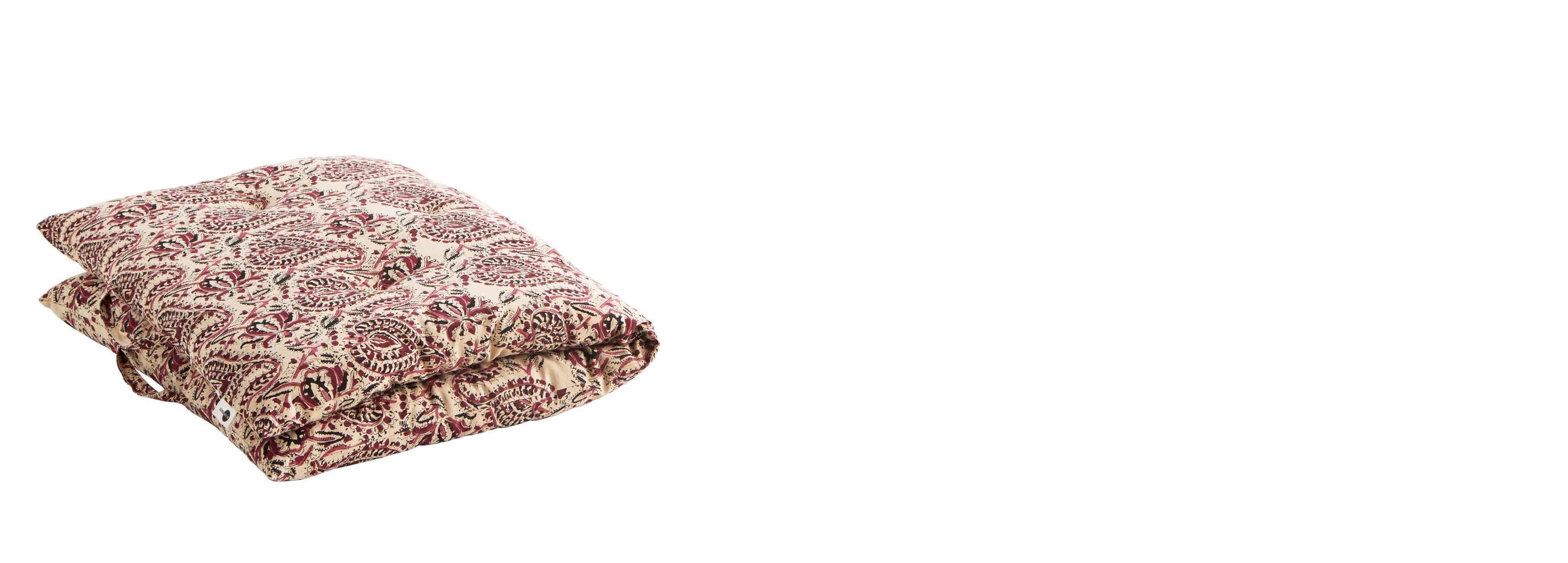 Block print floral mattress in raspberry, beige and black tones folded over with handles visible on white background