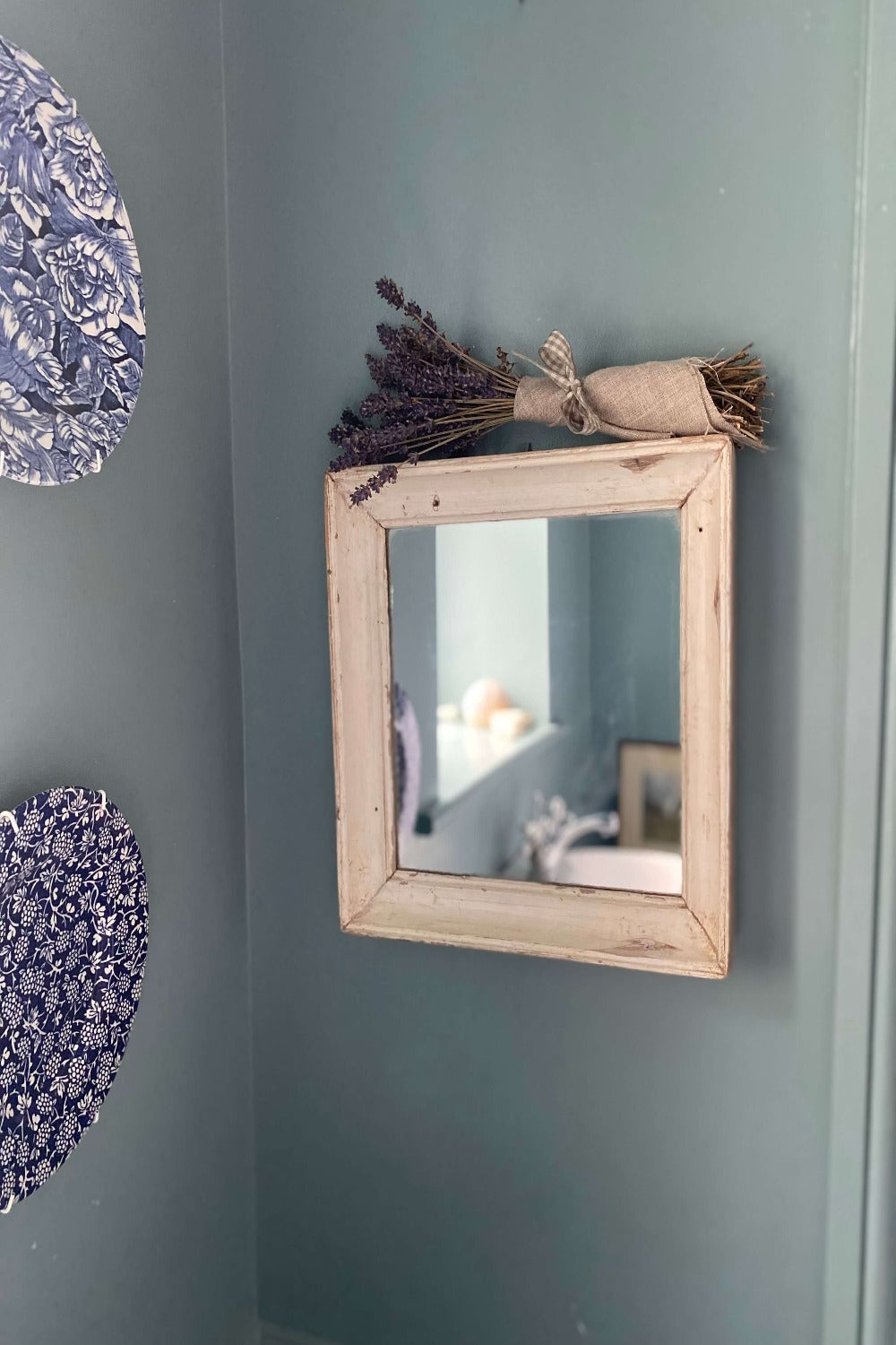 Reclaimed white wood mirror in blue bathroom next to vintage plates