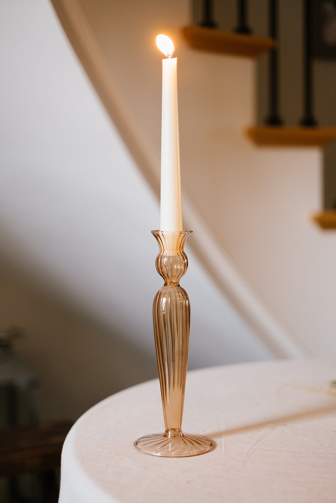 Rust fluted candle holder on a table in front of a stairs