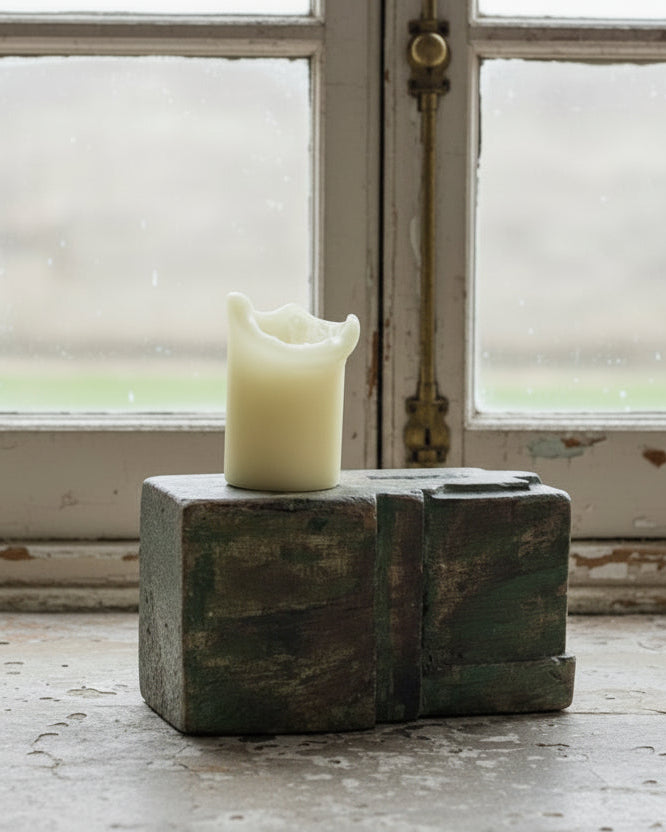 A rustic, dark green repurposed reclaimed wood candle holder with a pillar candle on top, set against a wooden background.