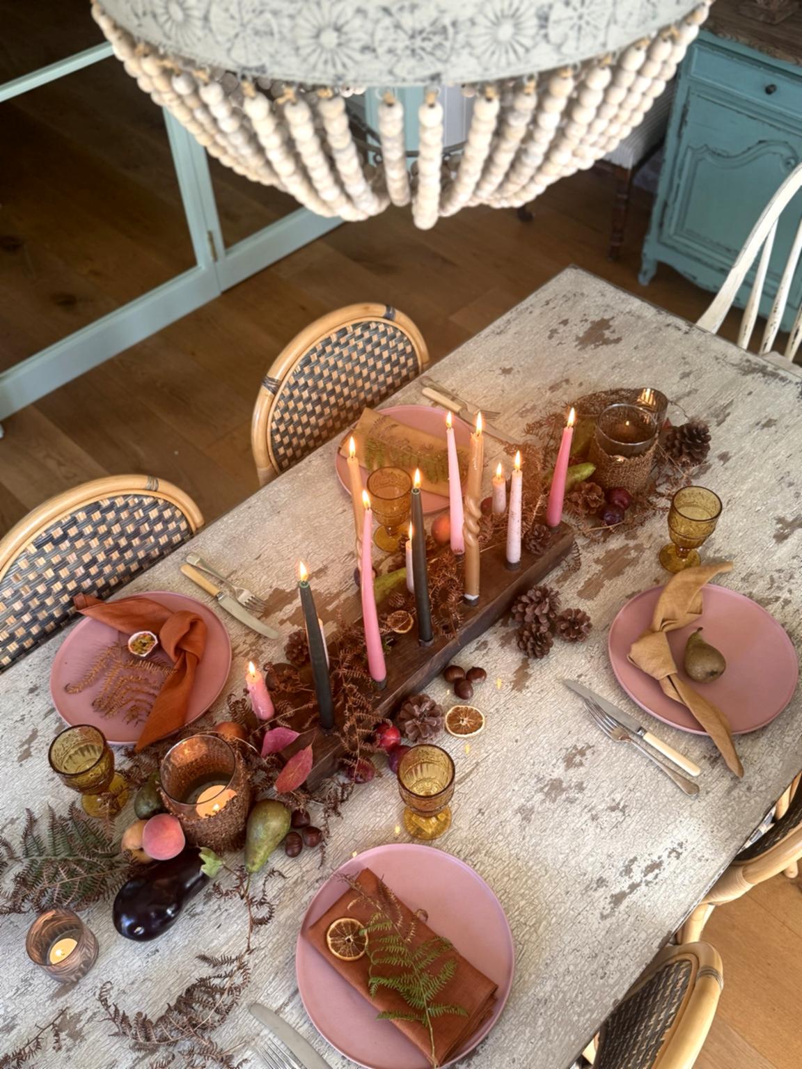 Decorative table setting with candles, pink plates, and gold accents in a rustic room.