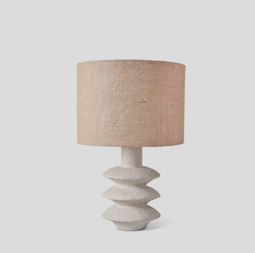 The Akito lamp with a creamy hued textured base and a jute lampshade, on a white background