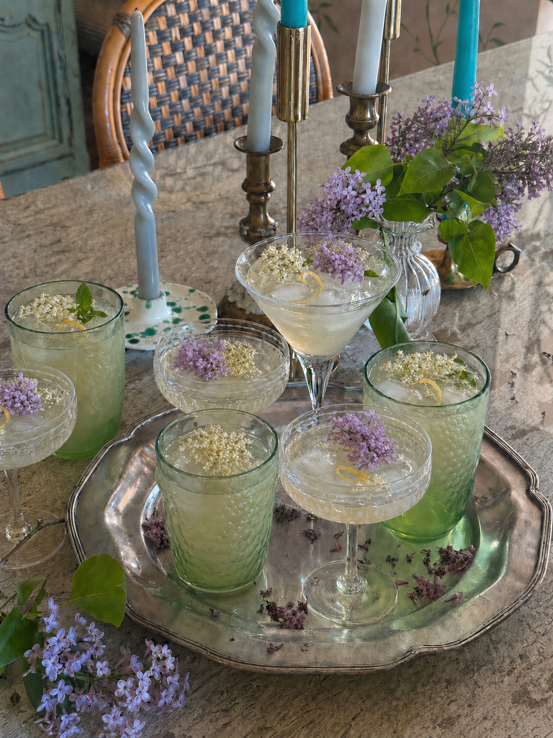 Antique tarnished silver tray of lilac and elderflower gin cocktails on a rustic white wood table with fresh lilacs and candles