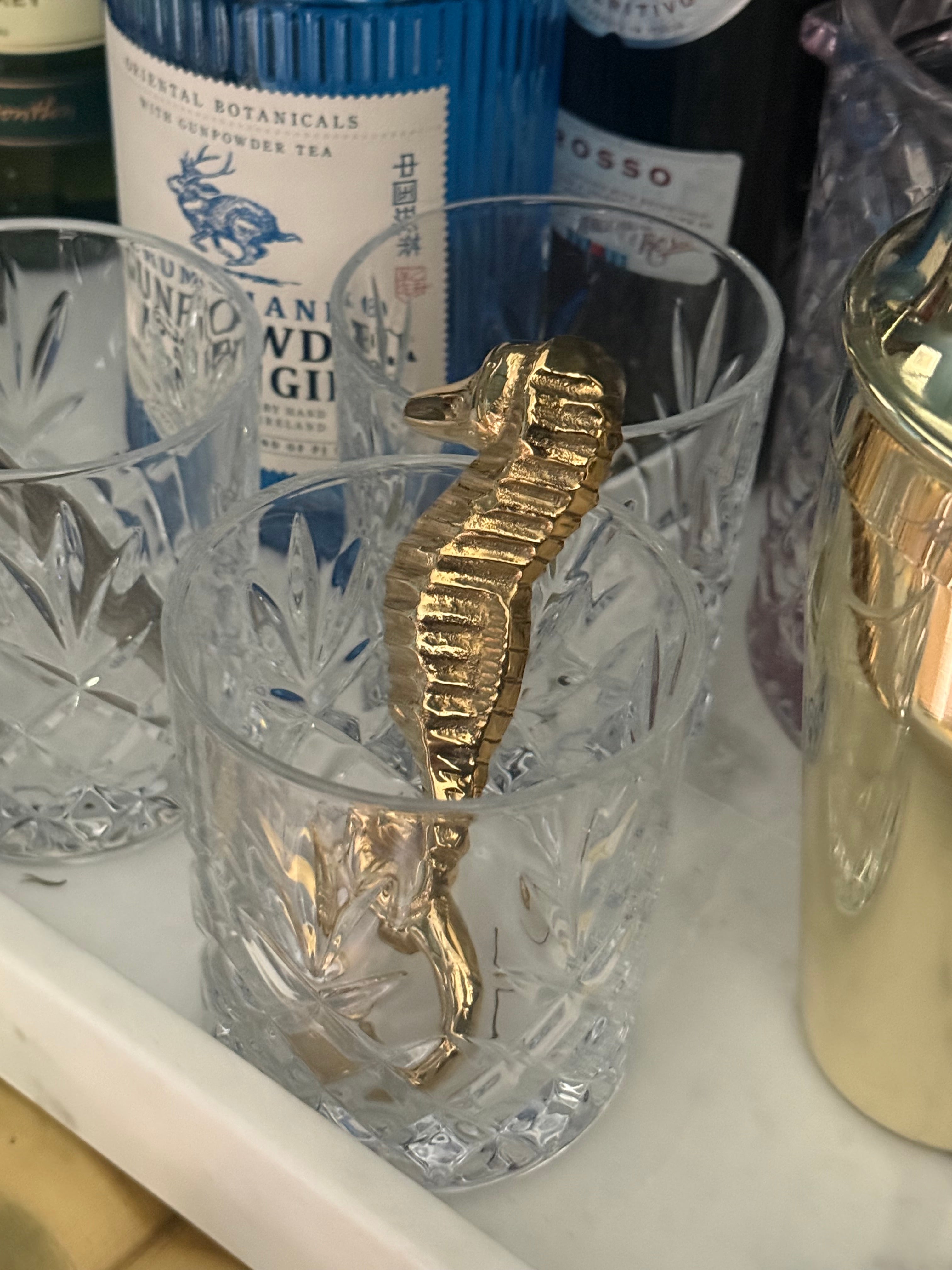 Cocktail glass with a gold sea horse bottle opener on white Marble tray with gin bottle and other spirits 