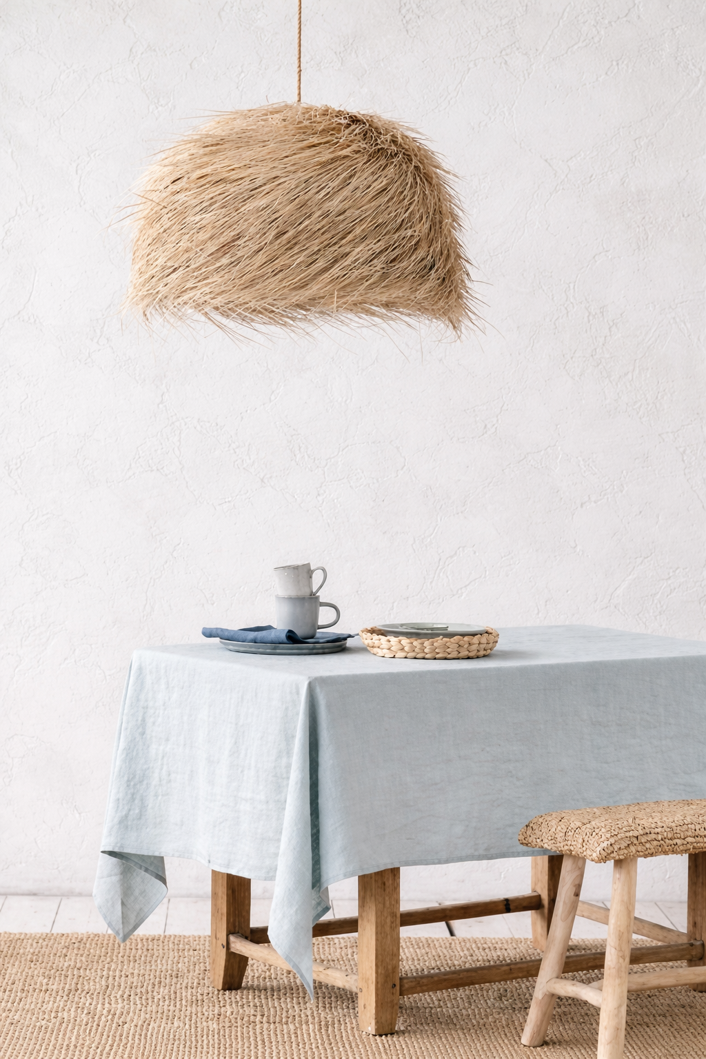 Dining room with a duck egg  blue tablecloth with oversized woven pendant light against textured white wall.