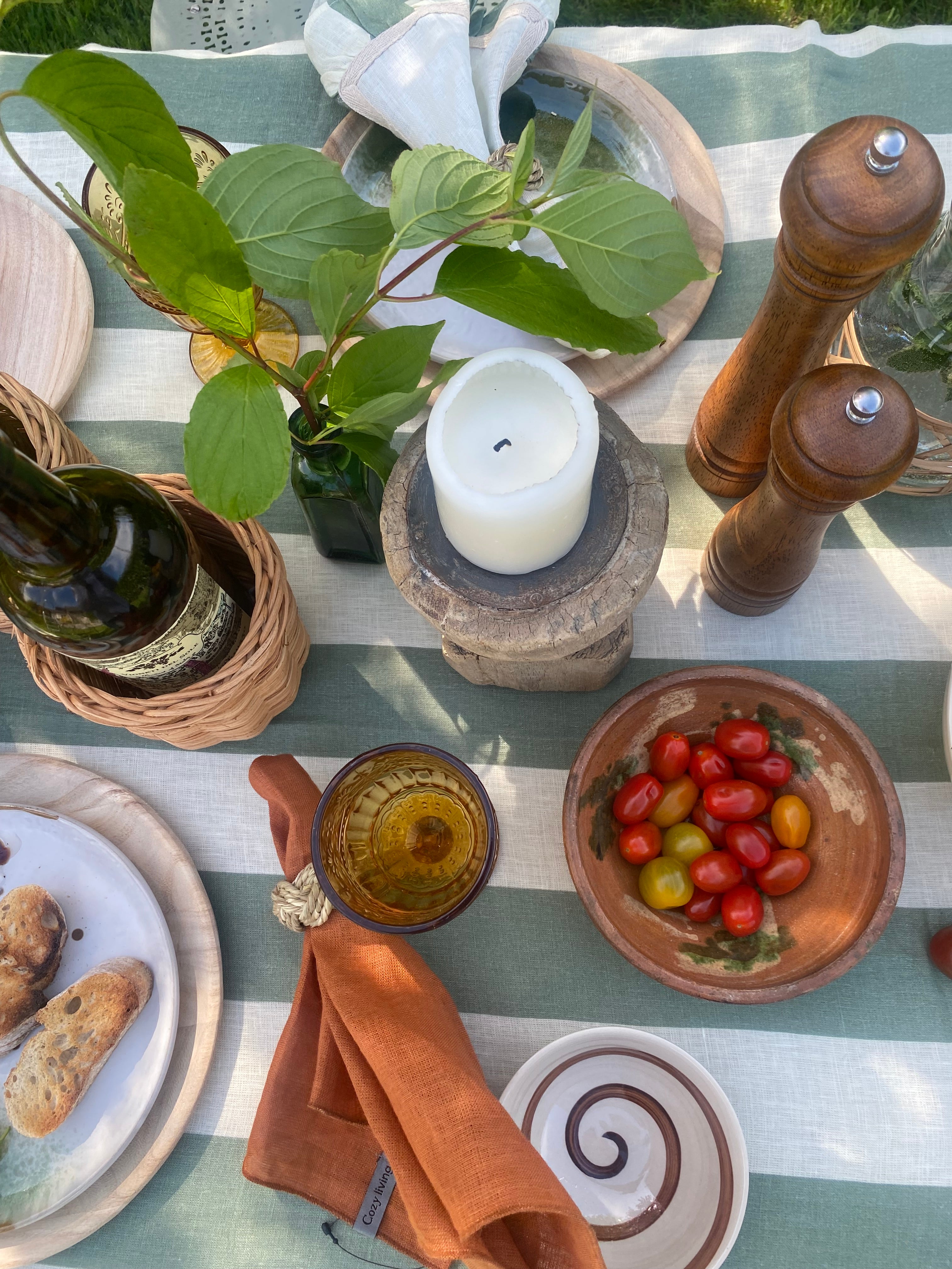 Table setting with a candle, bottle, bowl of tomatoes, and plates on a striped tablecloth.