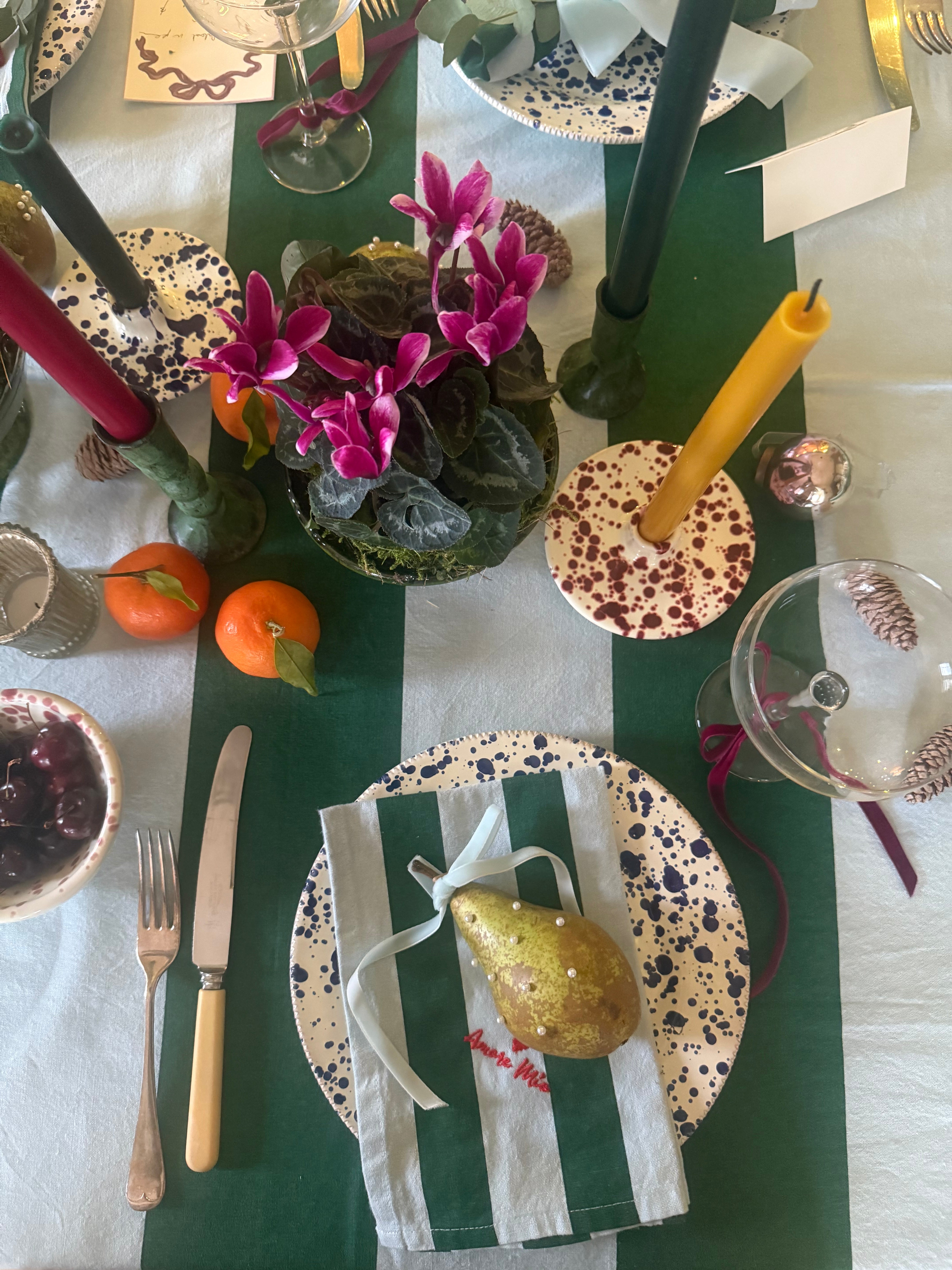 Dining table setting with green and light blue tablecloth, blue splatter dinner plate, striped napkin, pearl encrusted pear place setting, cutlery, and decorative items.