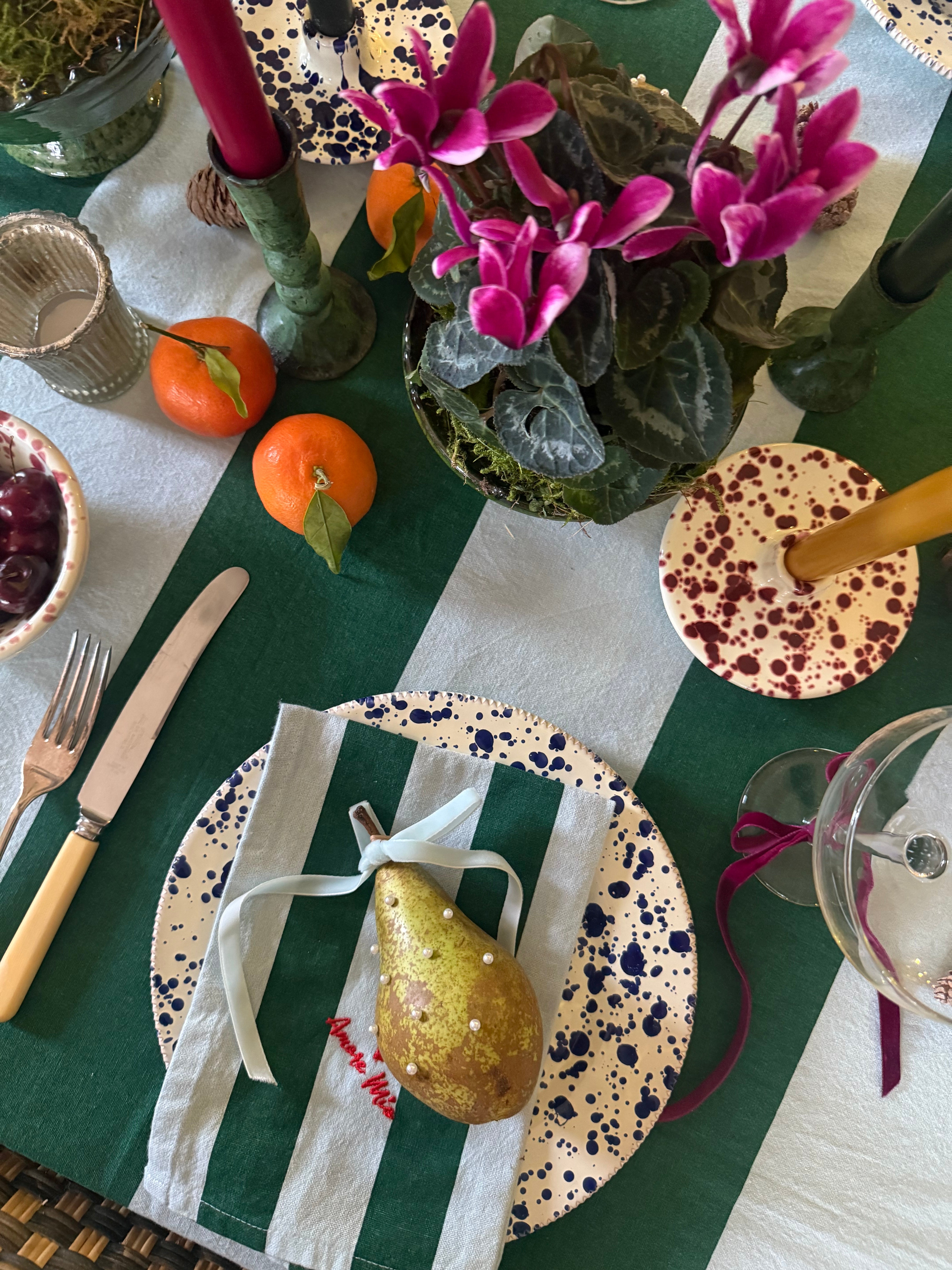 Decorative table setting with blue splatter plates, candles, and fruit on a light blue and green striped tablecloth.