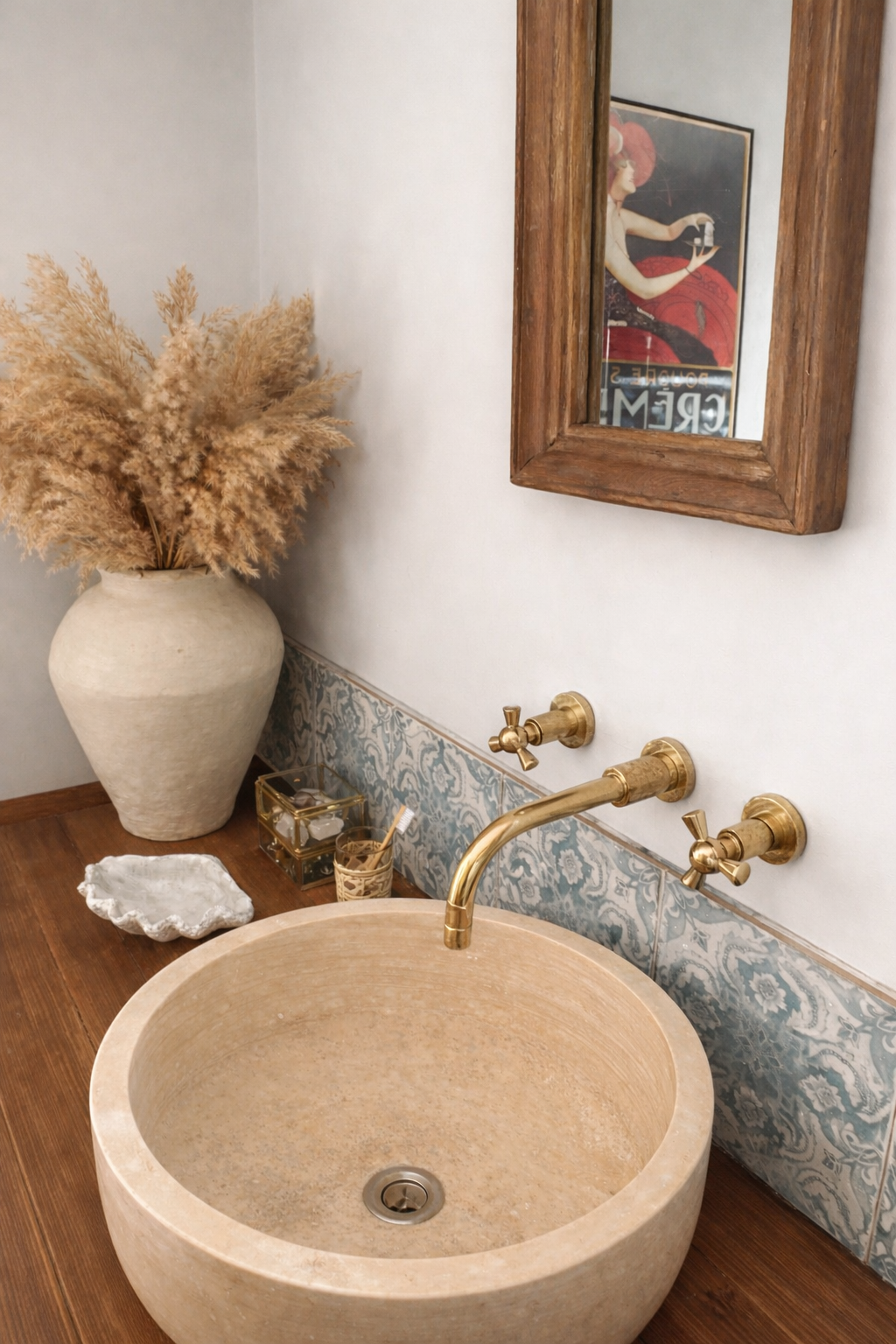 Bathroom vanity with stone sink, reclaimed mirror above, gold faucet, vintage blue patterned tiles, and decorative elements.