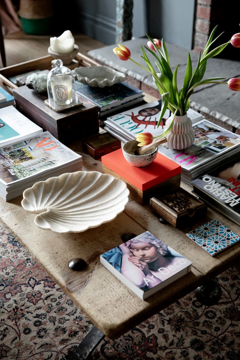 Decorative coffee table with books, a shell platter, and tulips on a patterned rug.