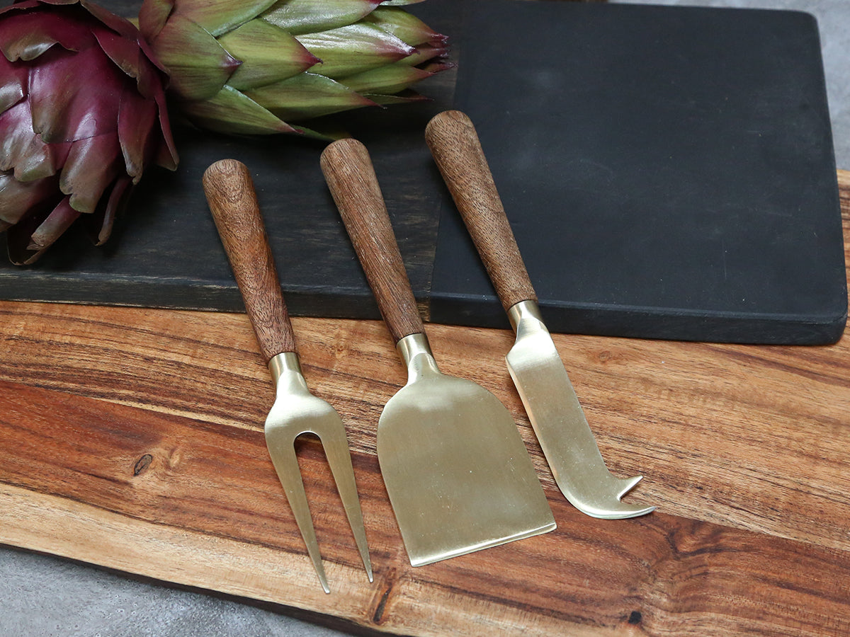 Set of brass cheese knives on a slate board on rustic wood surface