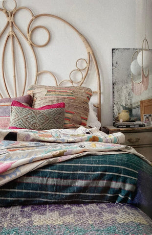 Bohemian styled bedroom with scrolled rattan headboard, vintage suzani on the bed with colourful cushions next to a pink fringed pendant lamp