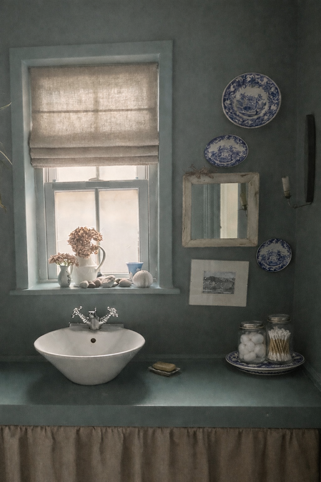 Vintage-style bathroom with a sink, reclaimed wood white mirror, natural linen roman blind and natural linen curtain and decorative plates on a dark blue wall.