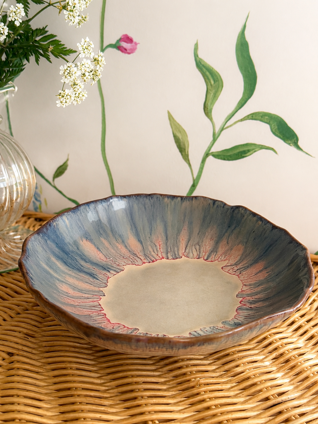 Close up of watercolour footed bowl with blue, pink and purple glaze on rattan surface against hand painted mural