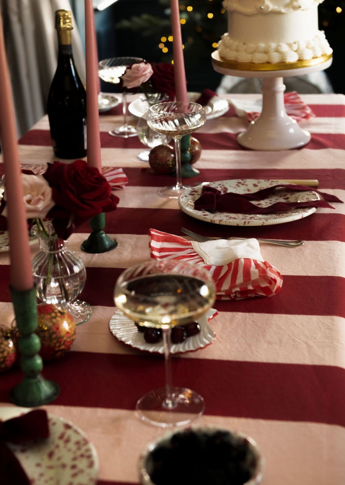 Decorative table setting with candles, wine glasses, and a cake on a red and white striped tablecloth.