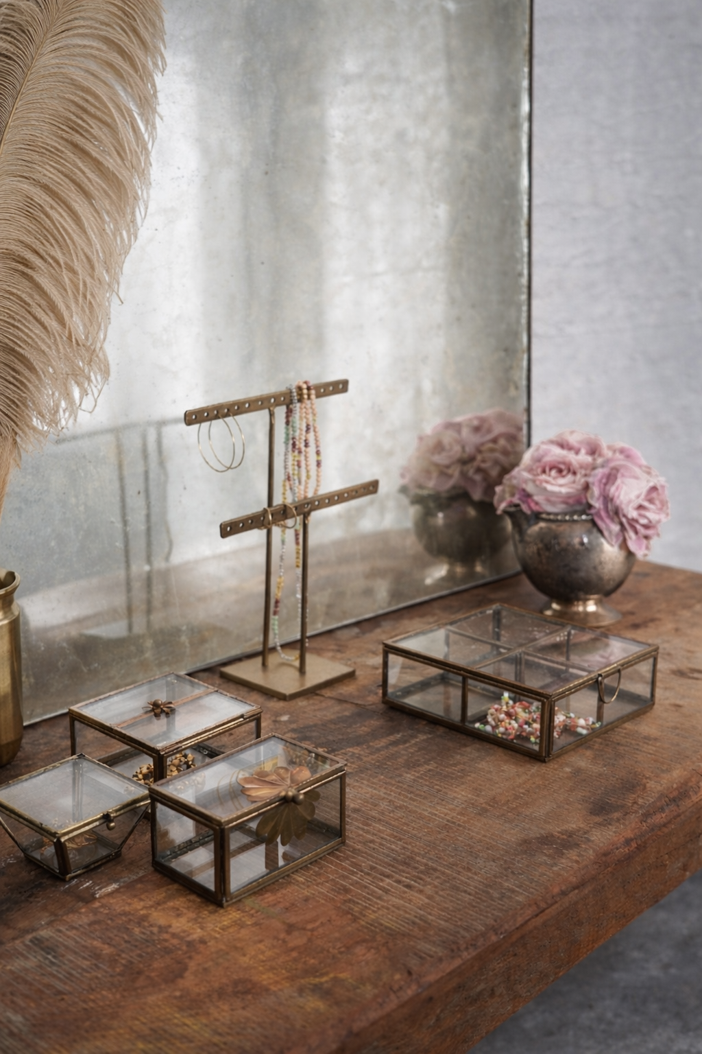 Glass jewelry display cases on a wooden surface with a mirror and flowers in the background.