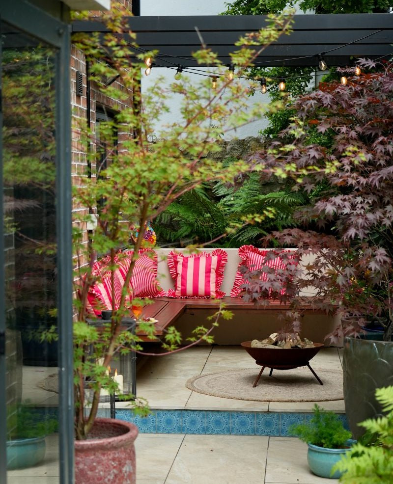 Cherry and peach striped cocktail cushions on corner bench in an urban city garden design with a fire pit and turquoise riser tiles.