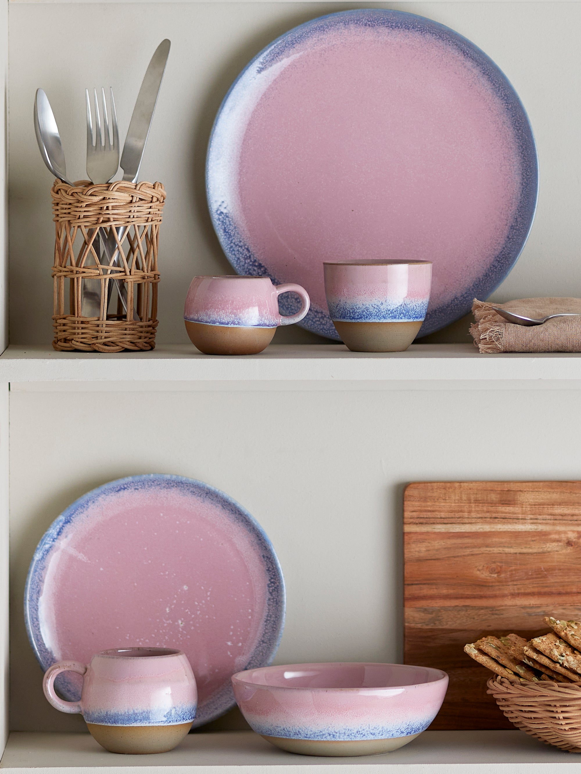 Ceramic tableware set with pink and blue rim on a shelf.