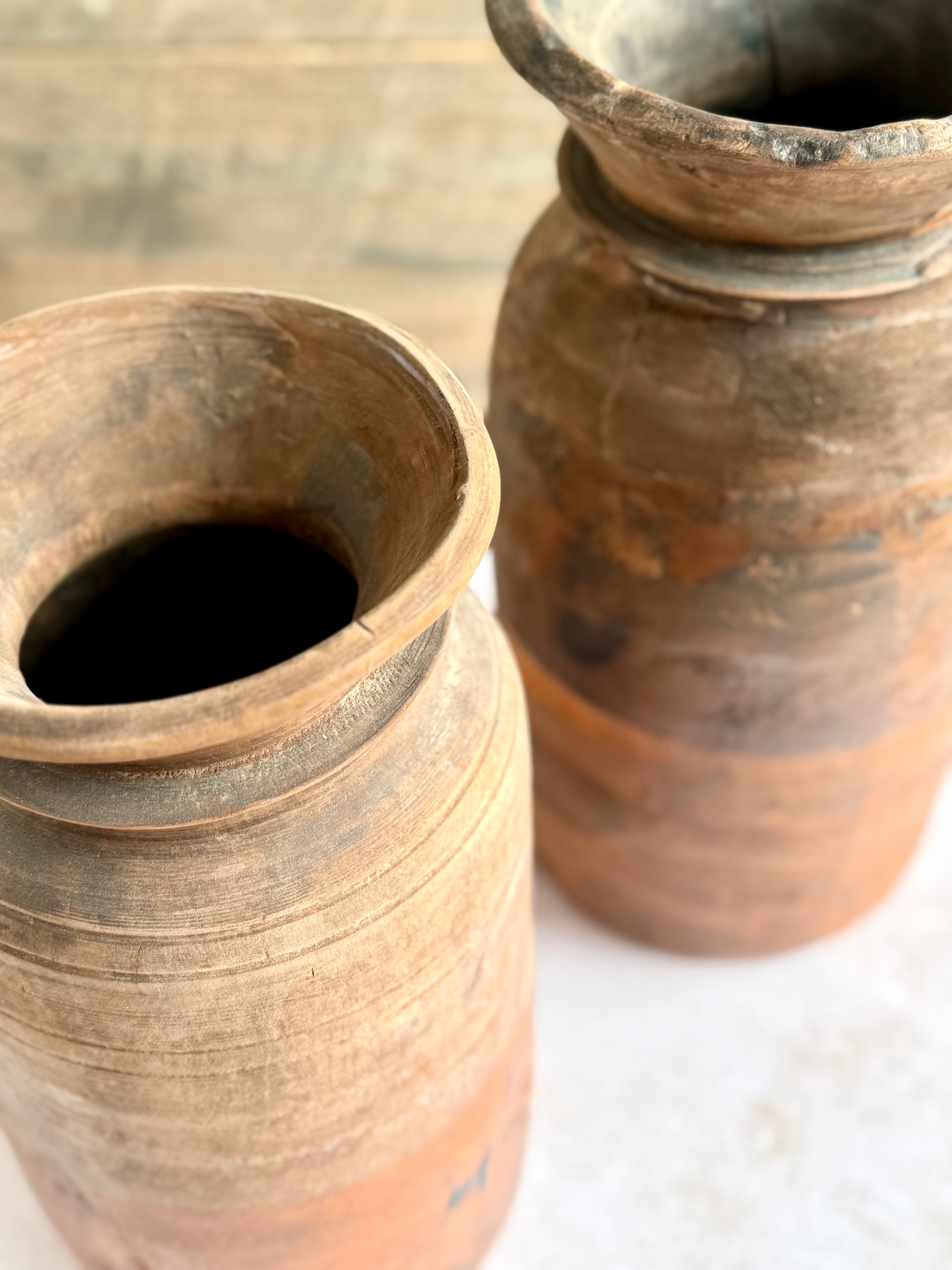 Two ancient clay pots with worn exteriors on a plain background.