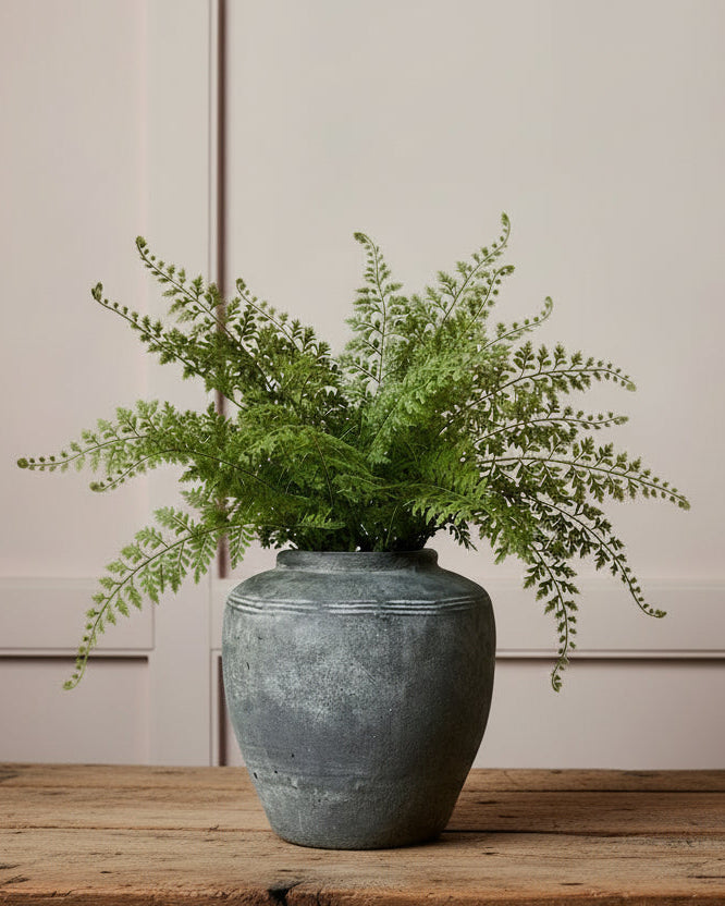 Grey cement vessel with fern on old wood table against chalky pink panelled wall