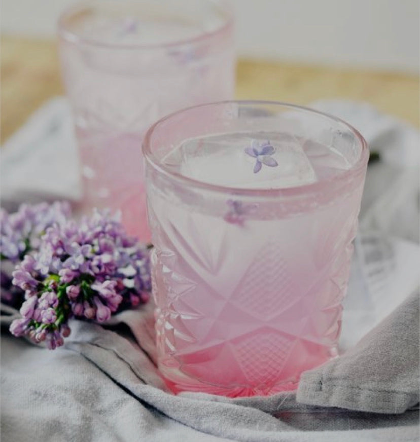 Pink and lavender cocktail in cut glass tumbler next to fresh lavender bunch