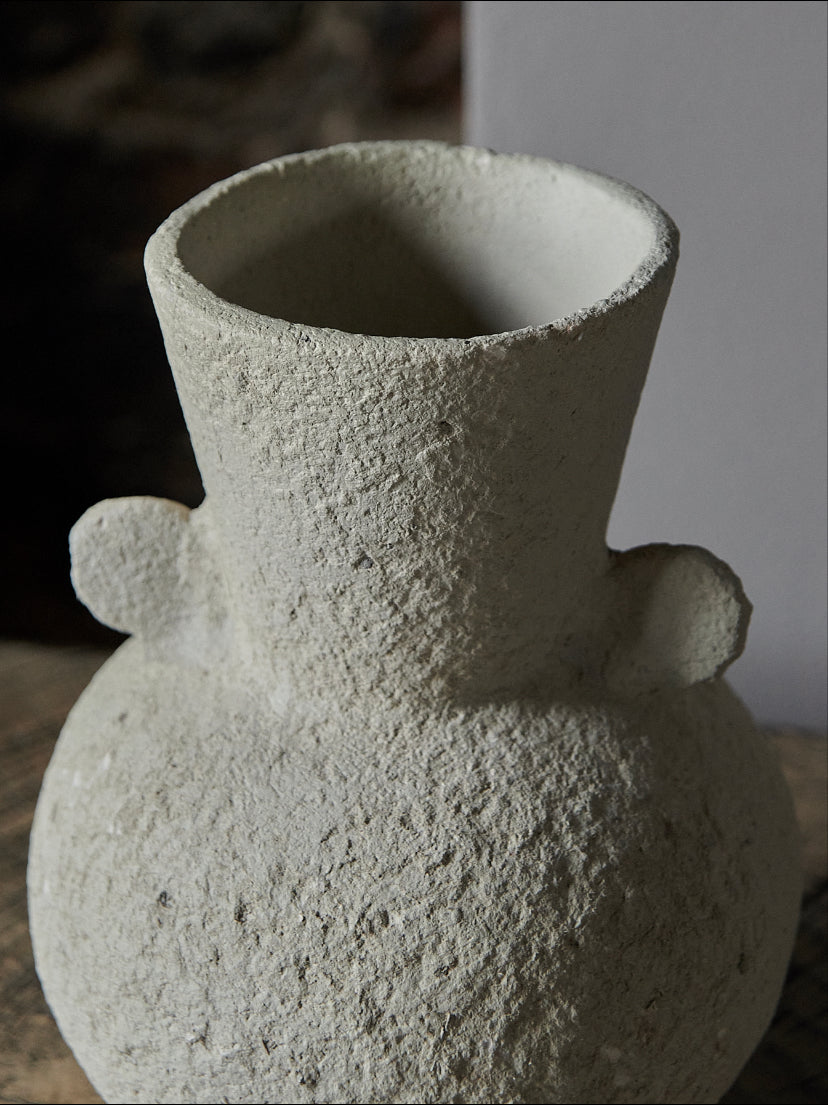 Textured cream vase with a curvy design, in soft creamy white beige tones, displayed on a rustic wooden sideboard 