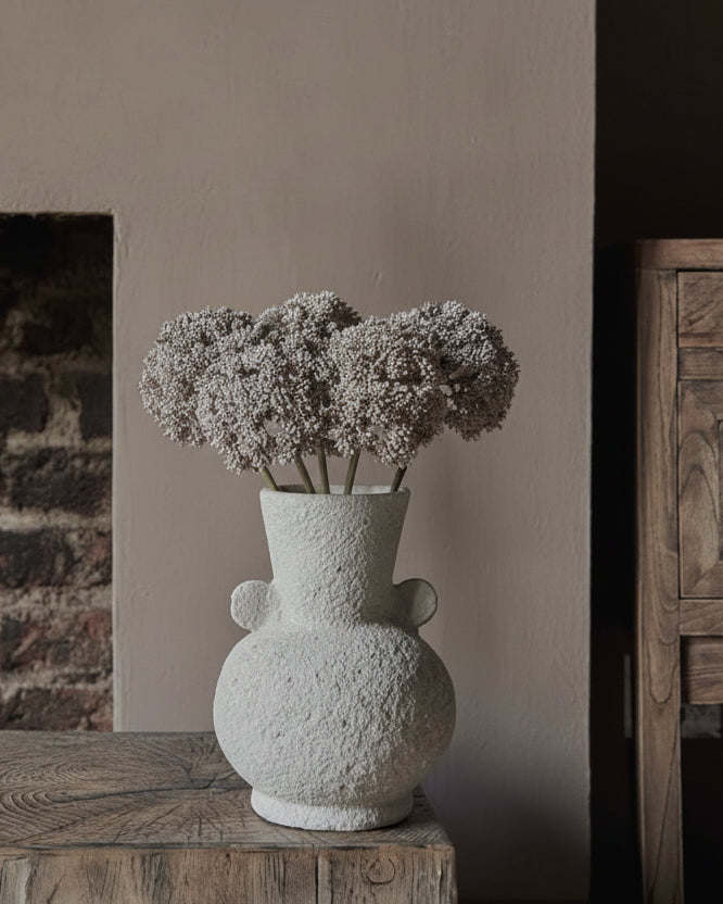 Creamy textured curvy vase on rustic wooden stool in warm living room
