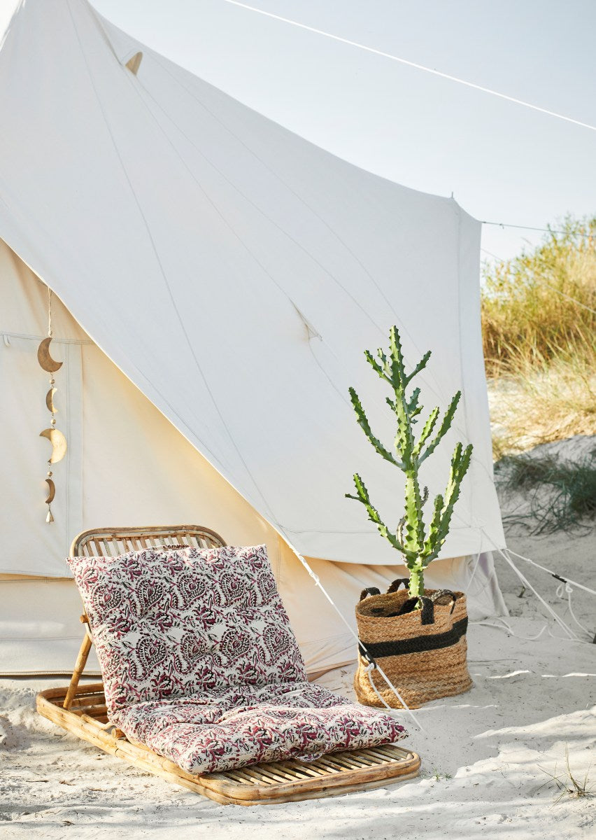 Camping chair with patterned cushions and a plant in front of a bell tent on a sandy beach.