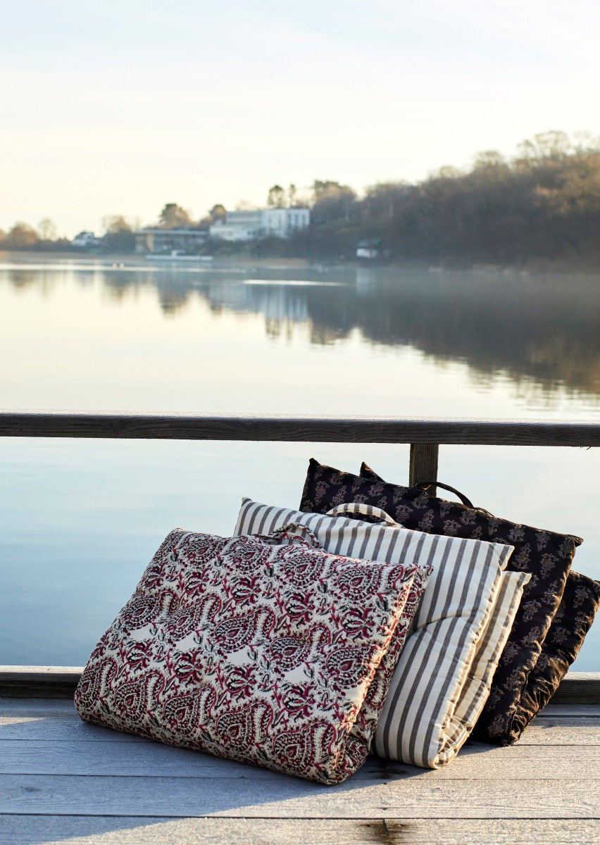 Folded printed seat mattresses with handles leaned against a balustrade overlooking a lake on a summer's day