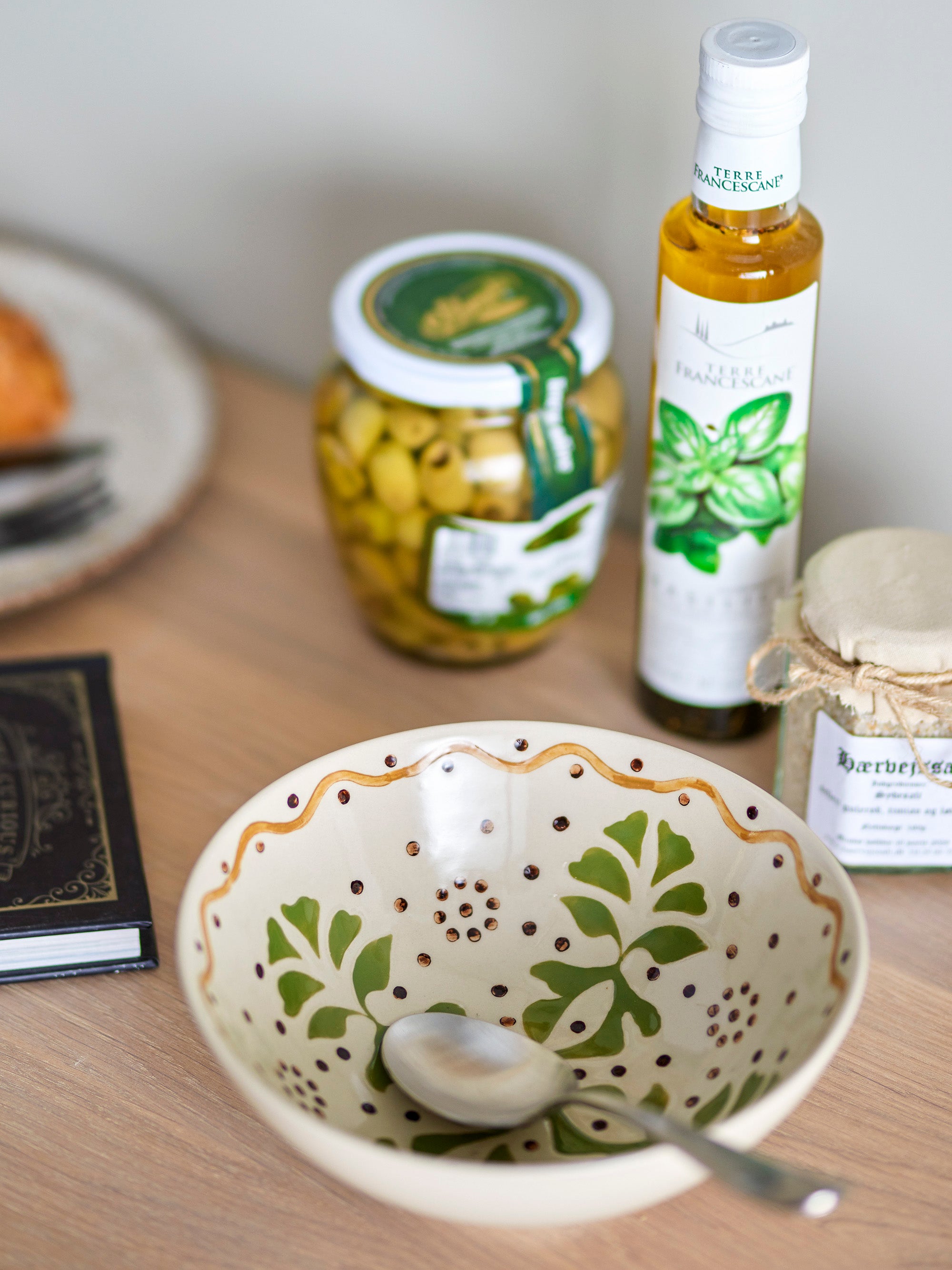 Handpainted ivory bowl with green and ochre tones on wood surface next to condiments