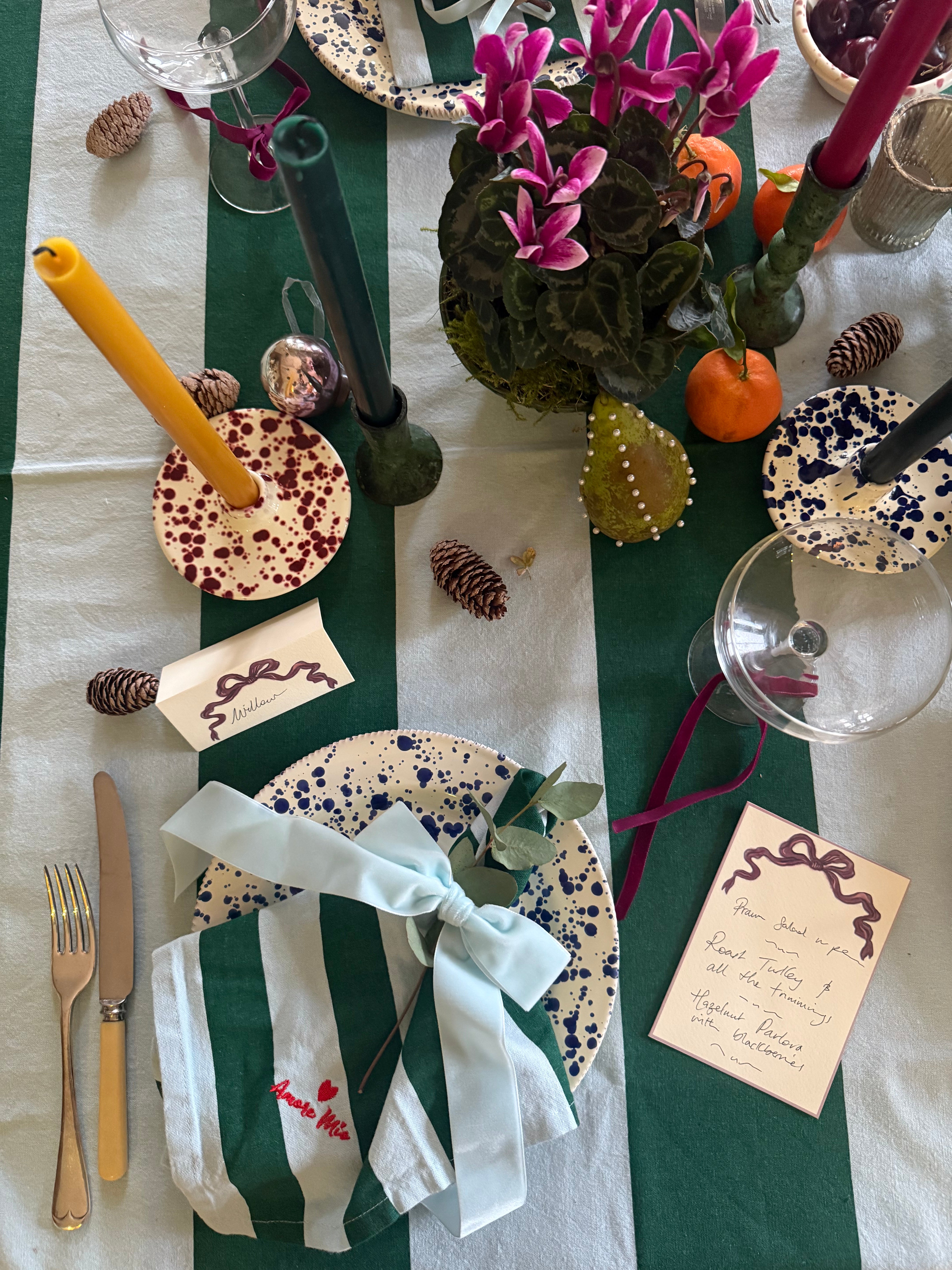 Decorative table setting with light blue and green striped tablecloth, blue splatter plates, light blue velvet napkin bow and cutlery.