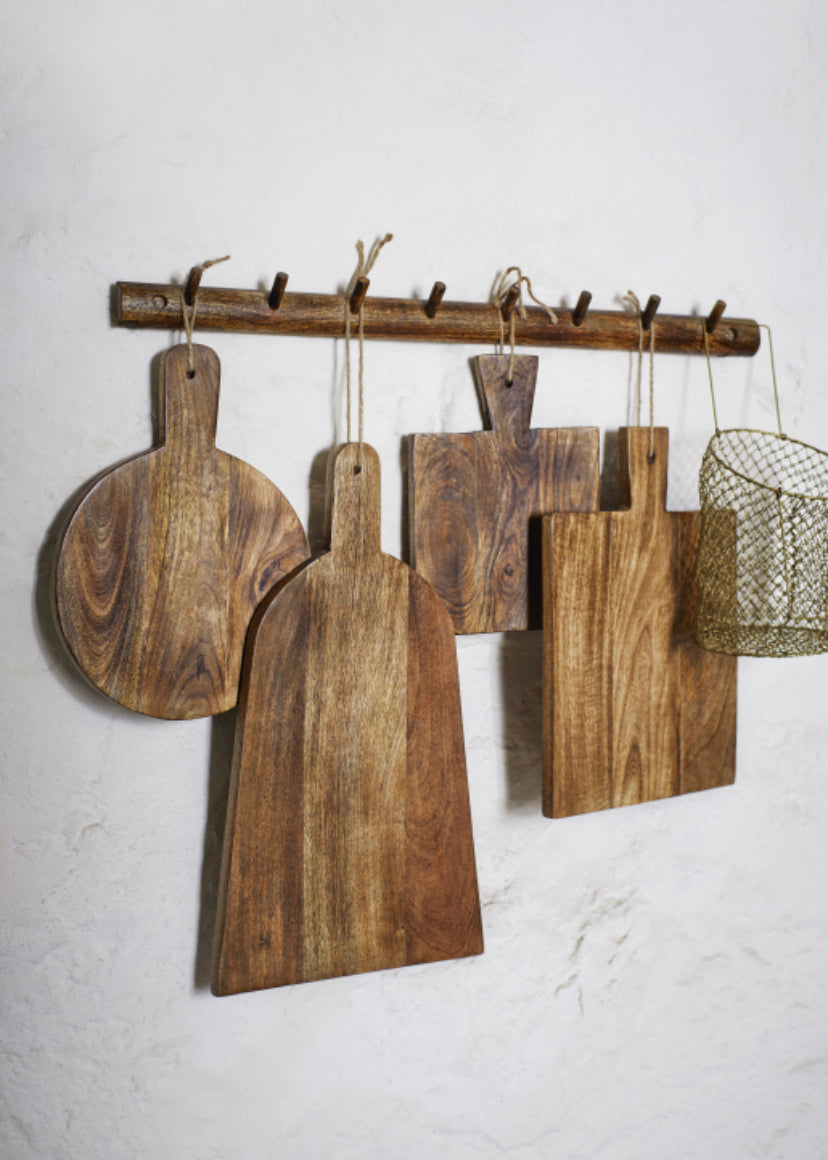 Collection of mango wood boards in different shapes and sizes hanging from wood hooks against white wall