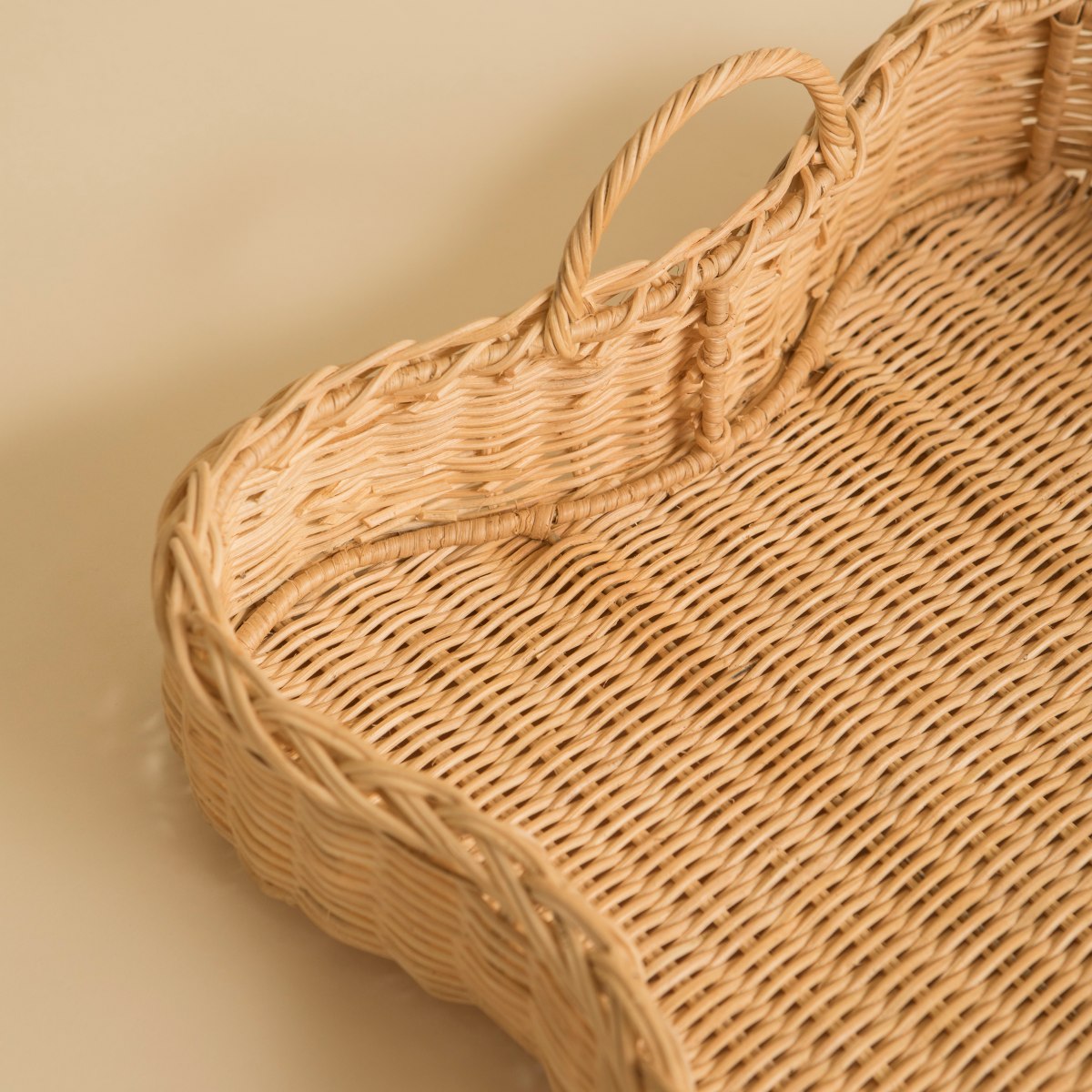 Woven scalloped rattan tray with a handle on a beige background