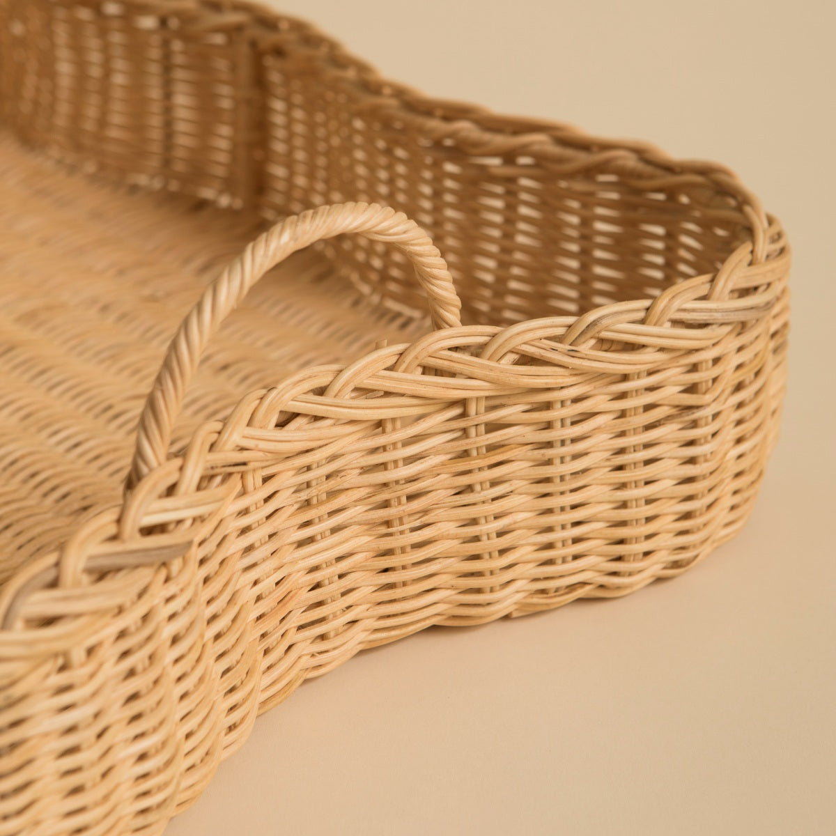 Woven scalloped rattan tray with handles on a beige background