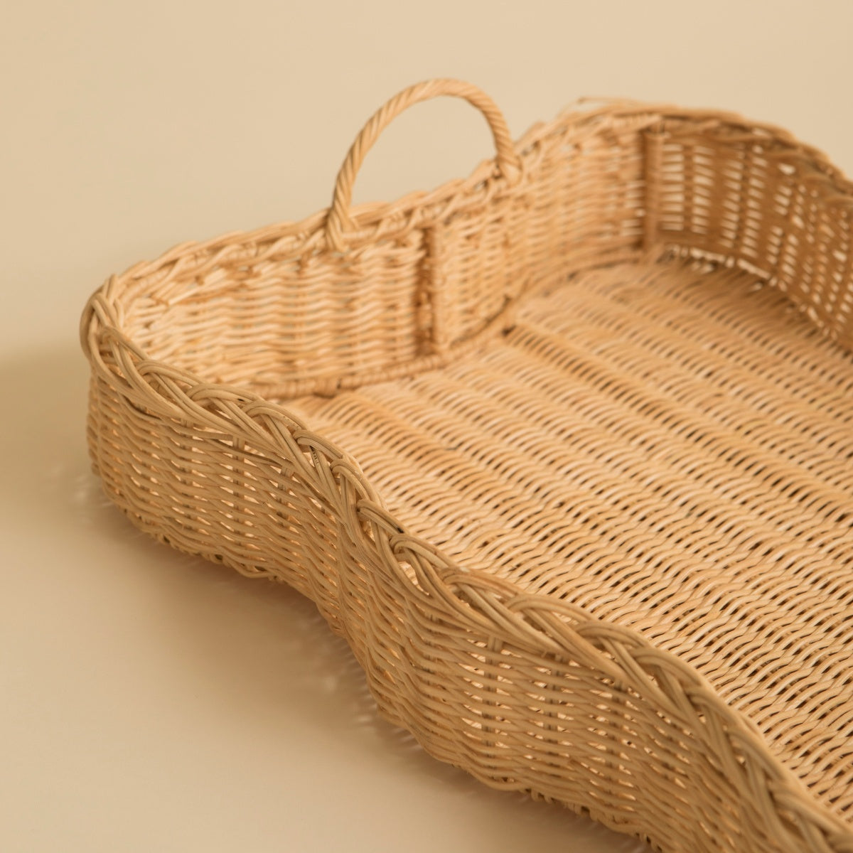 Woven scalloped rattan tray with a handle on a beige background