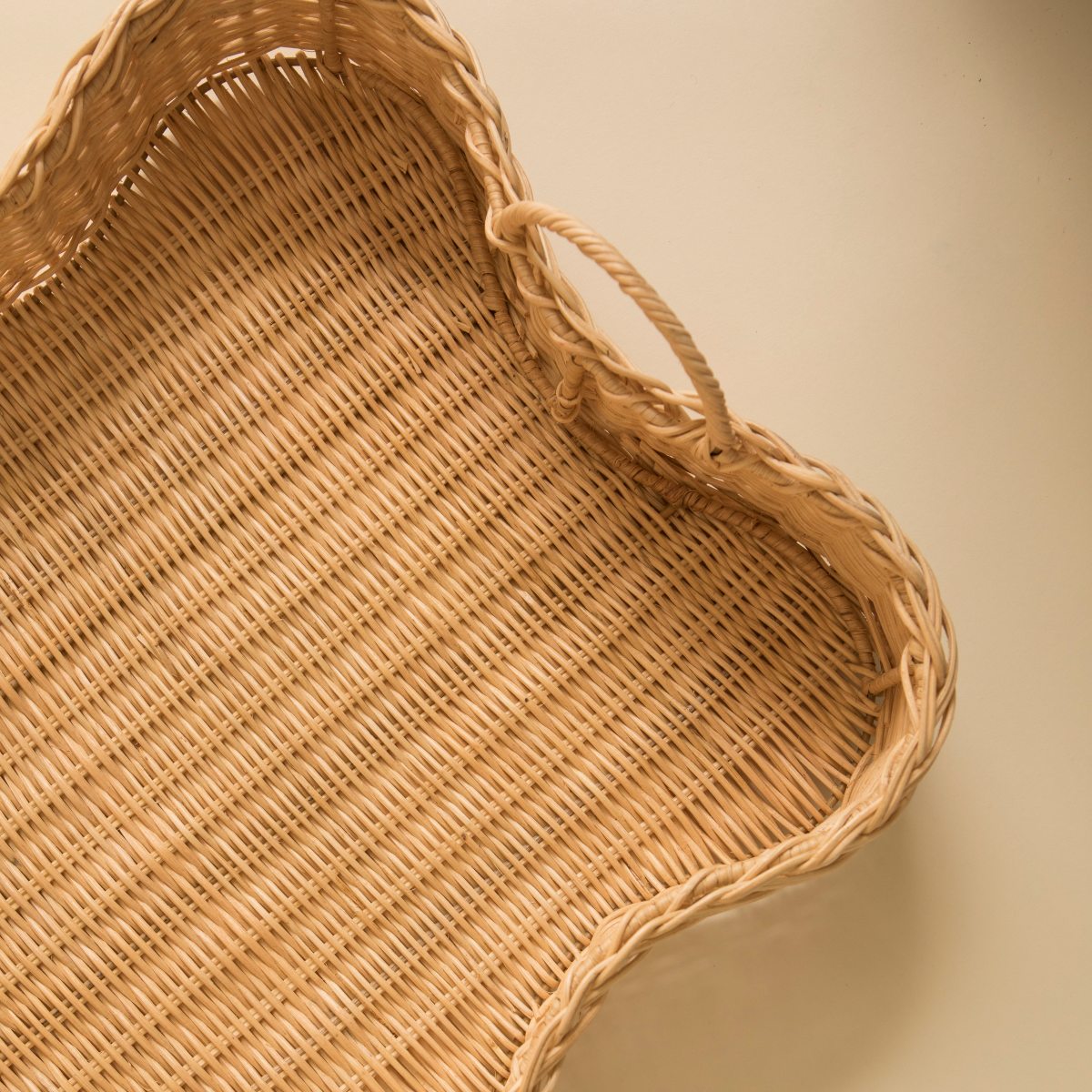 Close up detail of rattan scalloped tray with handles on a beige background