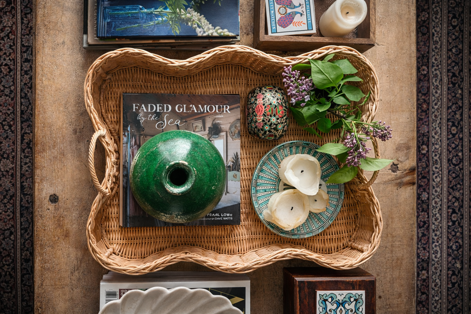 Scalloped rattan tray with decorative items including a green vase, candles, and books on a wooden surface.