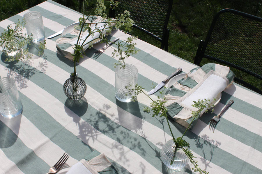 Sea green and off white linen table cloth on outdoor table with ruffled striped napkins and clear vases of greenery