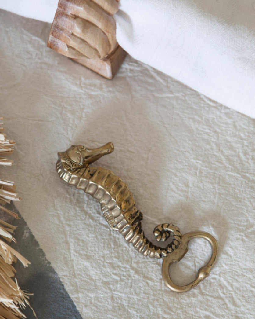 Brass seahorse bottle opener on a rumpled linen tablecloth 