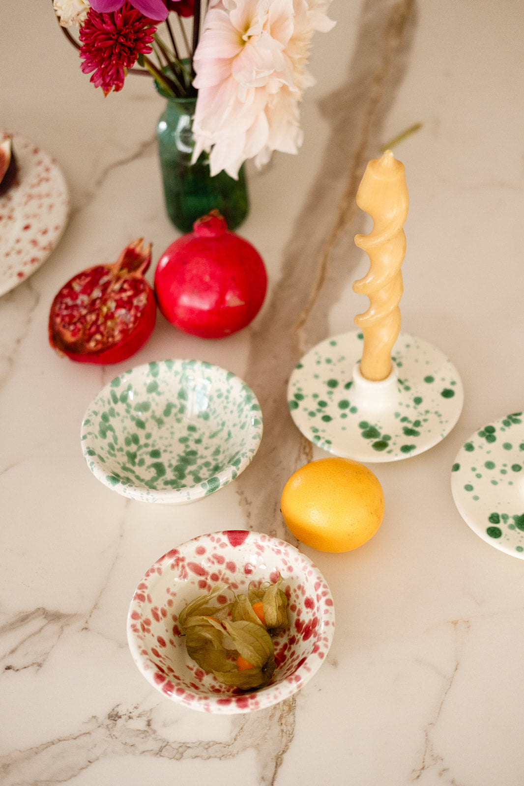 Shot of Italian green splatter bowl, green splattter candle holder, red splatter bowl on white marble surface